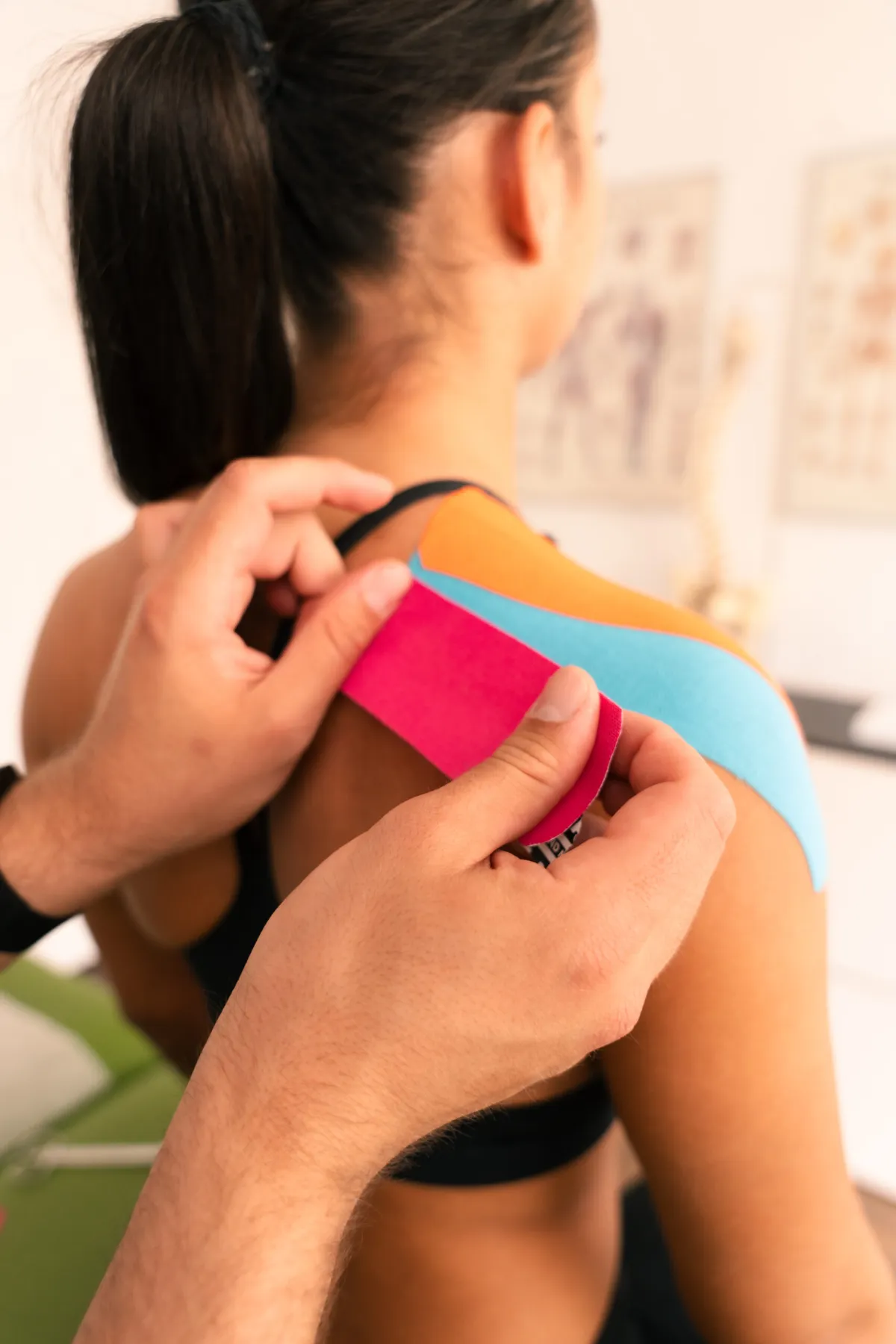 Anwendung von buntem Kinesio-Tape auf der Schulter einer Patientin.